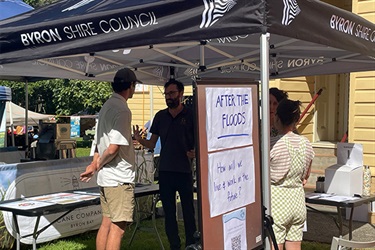 People talking to staff at market stall.