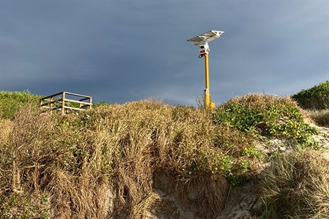 Emergency beacon, camera and solar panels mounted on pole on sand dune