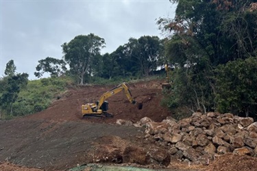 Large machine moving rocks on cleared land.