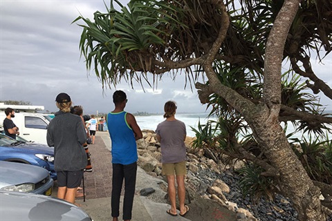 People standing on footpath looking at surf at Byron Bay