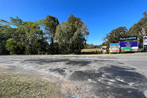 road that has potholes and patches with business signs in background