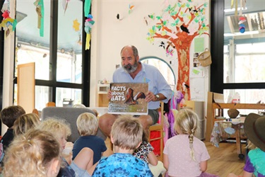 Council staff member reading book to small children seated on the ground.