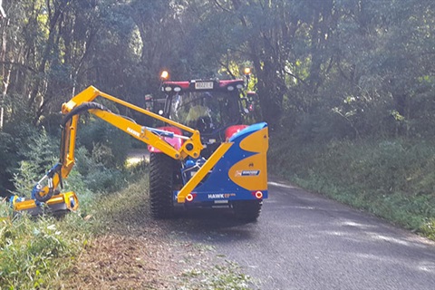 tractor with side arm slashing vegetation on narrow road
