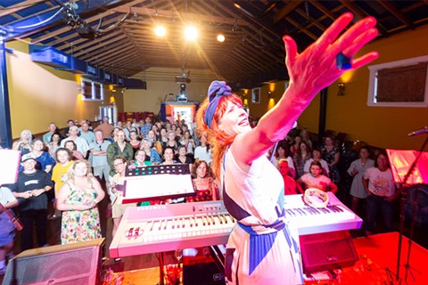 Performer on stage in front of a packed crowd. A key board and mcirophone is set up in front of them. 