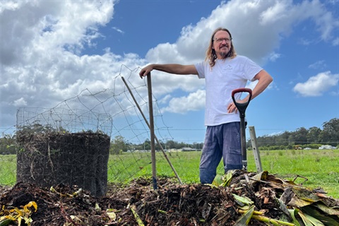 Person standing in front of a compost pile holding a spade