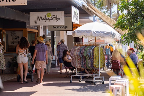 people on footpath looking at shops to left and rack of clothes on right of footpath