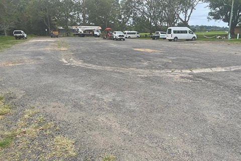 Gravel carpark with some potholes and cars, utes and lawn-mower in background