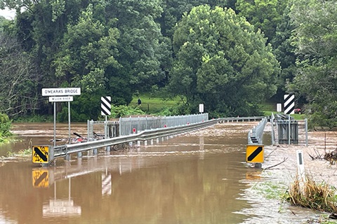 Sign showing O'Mearas Bridge covered in brown flood water with only railings visible