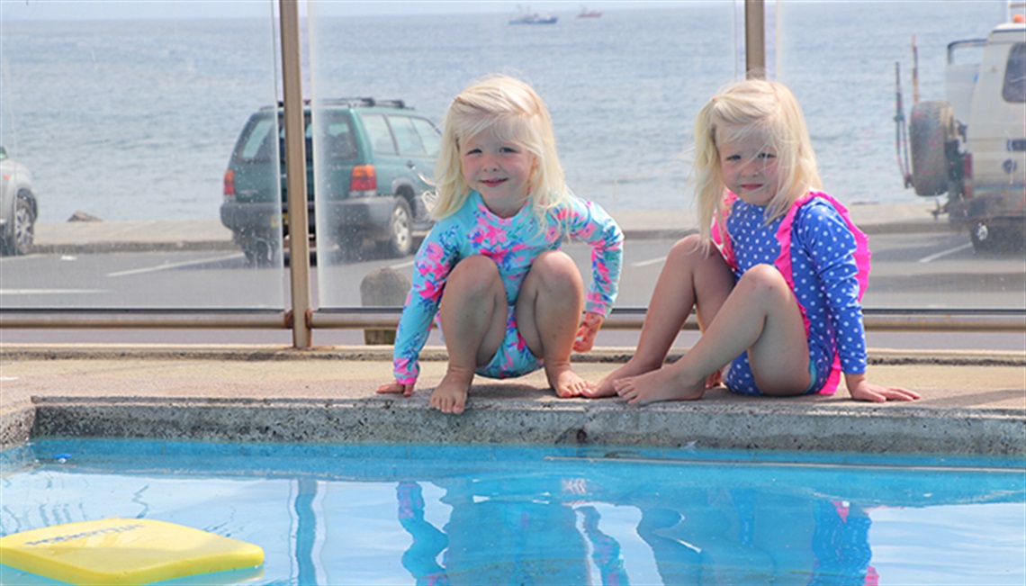 Two gilrs sitting on the side of the Byron Bay swimming pool