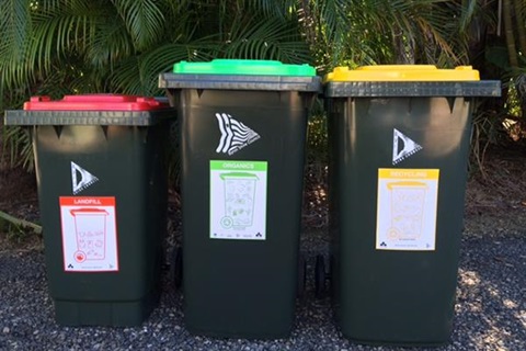 A red, green and yellow wheelie bin placed together on the side of the road. 